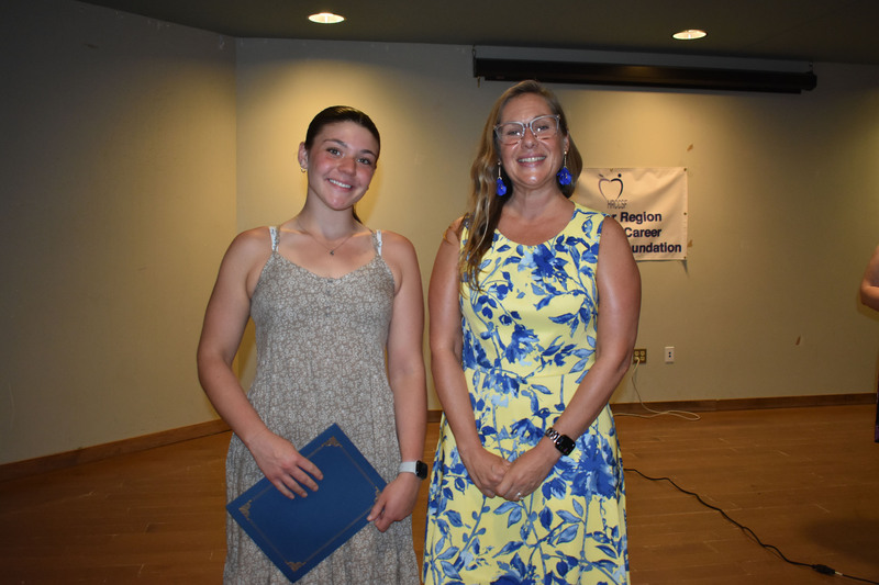 Student on stage holding certificate next to Sarah Crowe