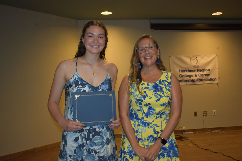 Student on stage holding certificate next to Sarah Crowe