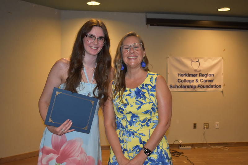 Student on stage holding certificate next to Sarah Crowe