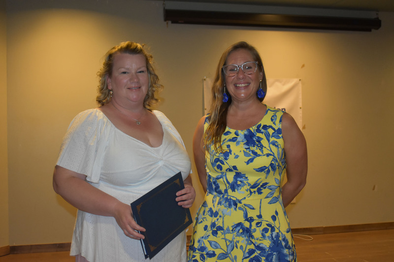 Student on stage holding certificate next to Sarah Crowe