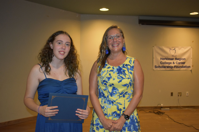Student on stage holding certificate next to Sarah Crowe