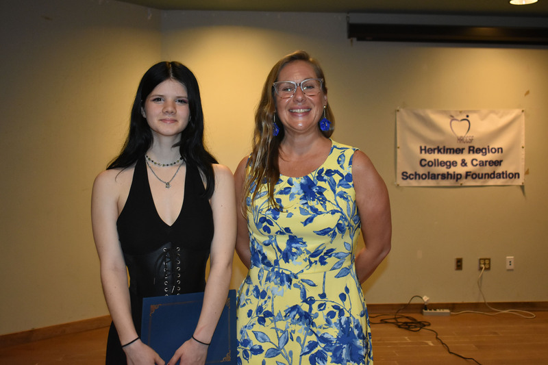 Student on stage holding certificate next to Sarah Crowe