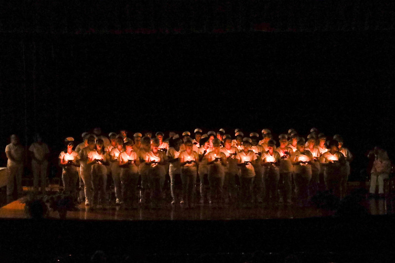 Adult LPN graduates standing on stage holding candles in a darkened auditorium for a candle-lighting ceremony