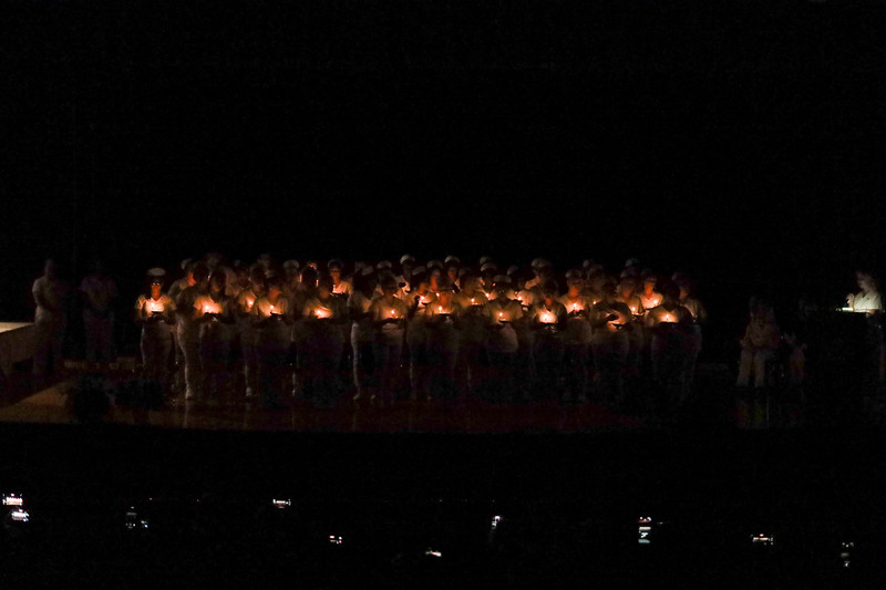 Adult LPN graduates standing on stage holding candles in a darkened auditorium for a candle-lighting ceremony