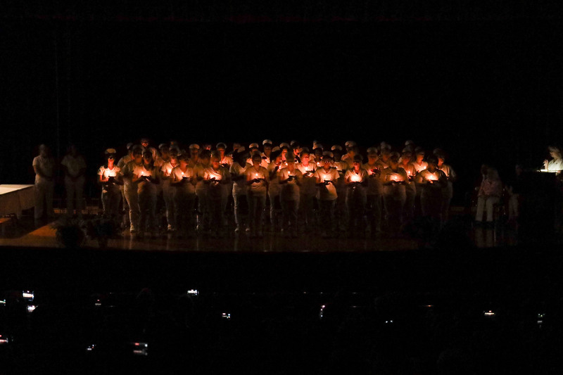 Adult LPN graduates standing on stage holding candles in a darkened auditorium for a candle-lighting ceremony
