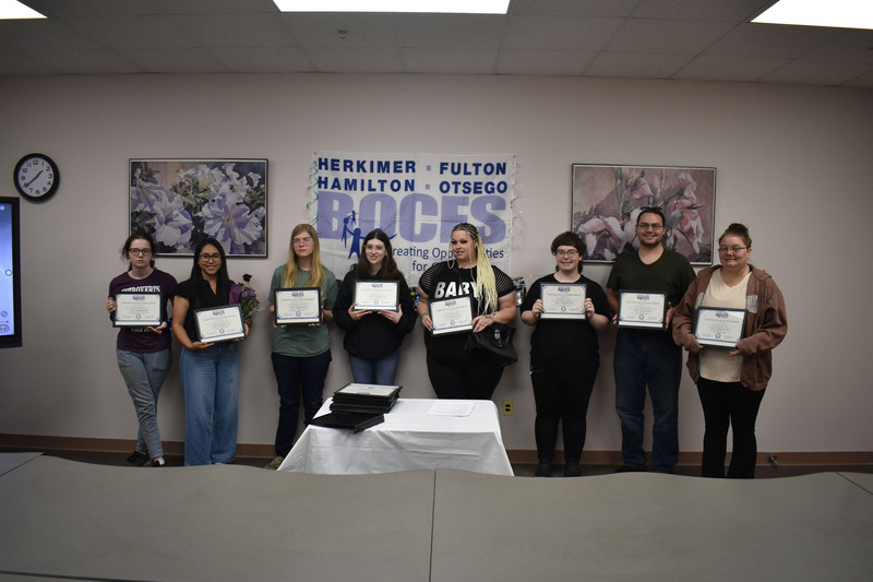Eight GED graduates posing with their diplomas in front of BOCES sign