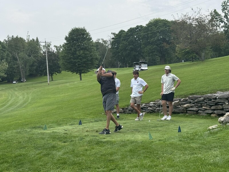DJ Shepardson swinging golf club on golf course as three others look on