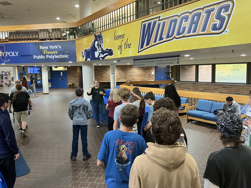 Students taking tour with tour guide at SUNY Poly with "home of the Wildcats" displayed on wall near them