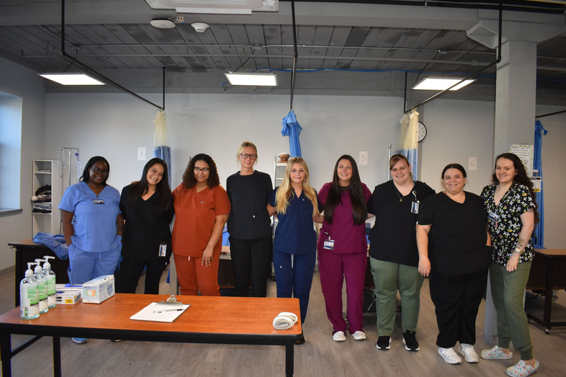 Nine adult LPN students posing together in practice lab