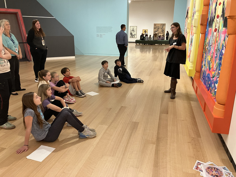 Students sitting and looking at paintings at art museum