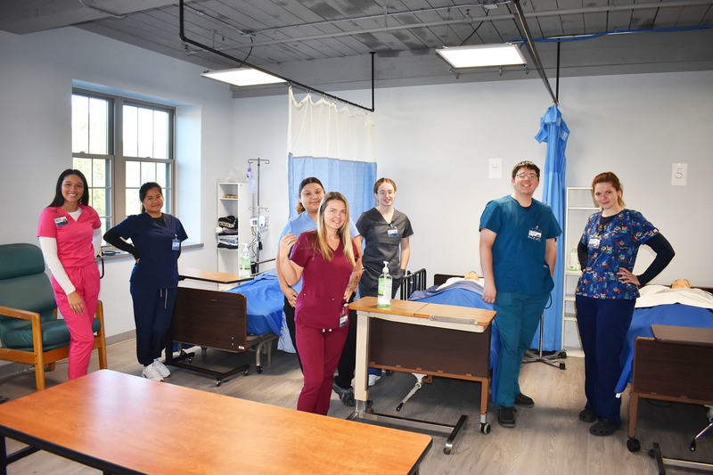 Seven adult LPN students posing in a nursing lab