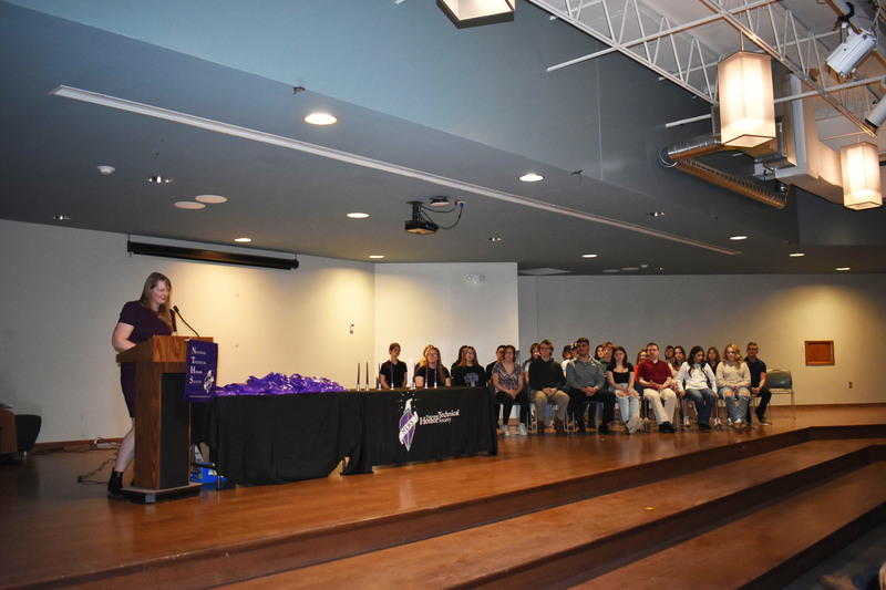 Sarah Schubert speaking on stage as NTHS inductees look on from chairs on stage
