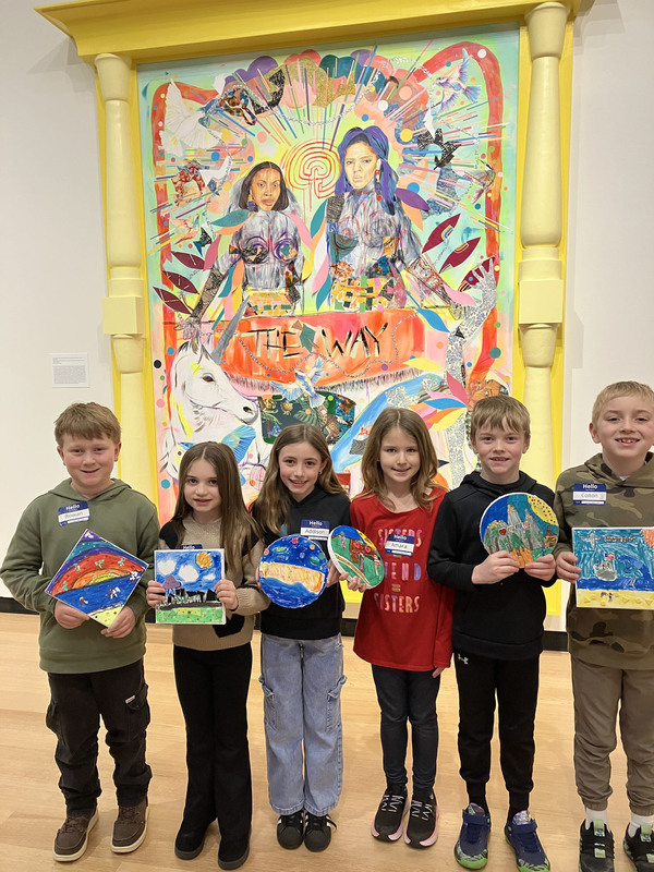 Students posing with artwork in front of larger art display at art museum
