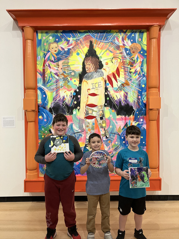 Students posing with artwork in front of larger art display at art museum