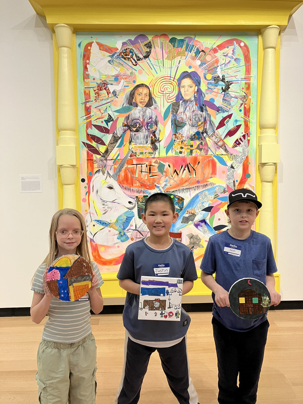 Students posing with artwork in front of larger art display at art museum