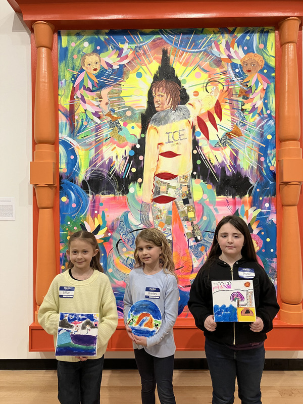 Students posing with artwork in front of larger art display at art museum
