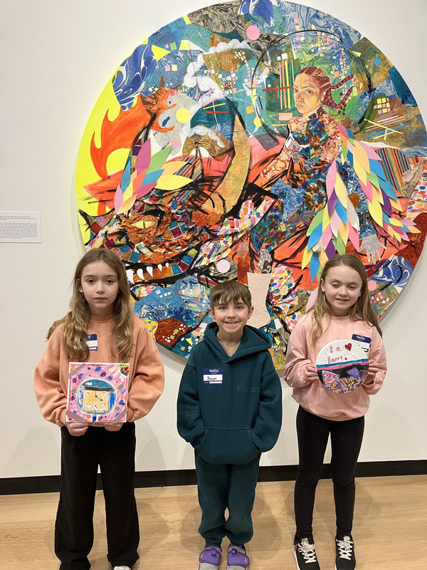 Students posing with artwork in front of larger art display at art museum