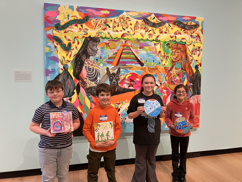 Students posing with artwork in front of larger art display at art museum