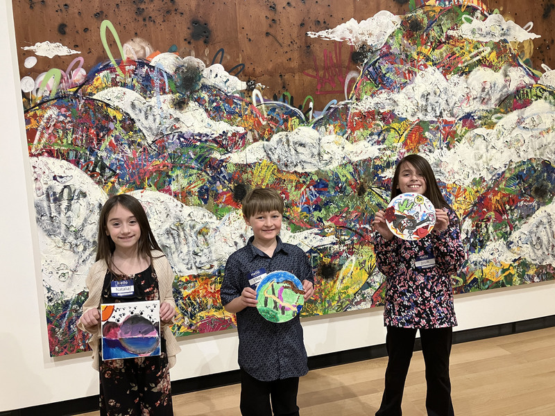 Students posing with artwork in front of larger art display at art museum