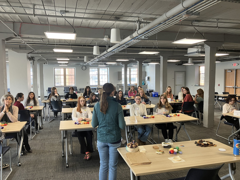 Back of artist speaking to large group of students who are sitting at tables