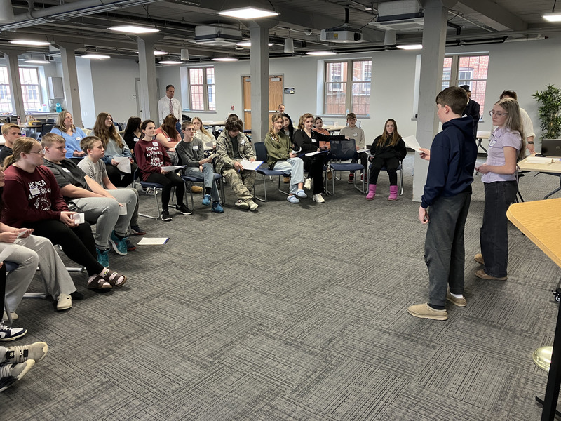 A few eighth graders standing and presenting to a room full of eighth graders