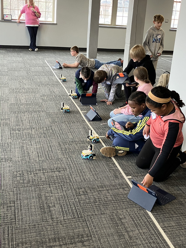 Students on floor operating robots with programming from tablets