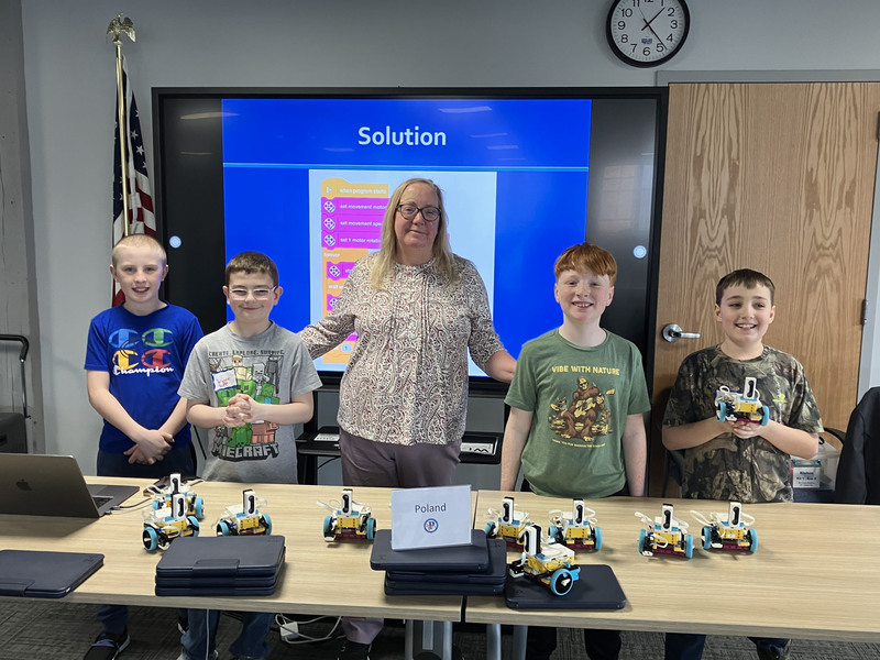 Students and teacher and presenter posing by table with robots and computers