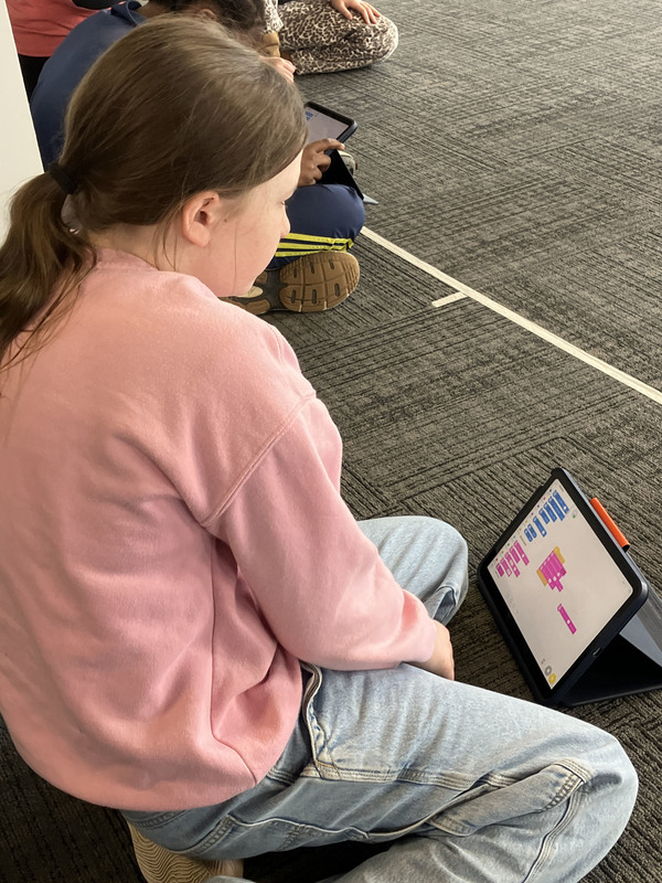 Students on floor using tablet by robot
