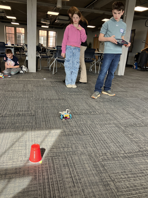 Students standing operating a robot with tablet