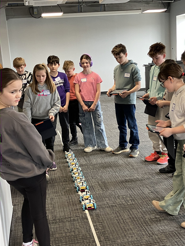 Students standing and using tablets to program robots