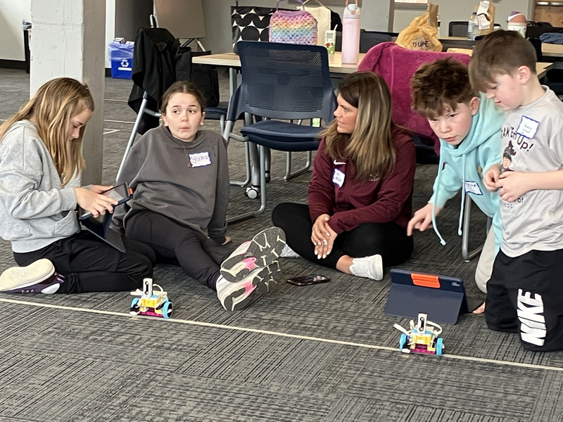 Students on floor with tablets and robots