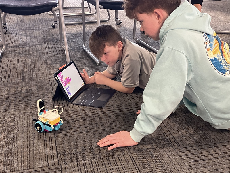 Students on floor with tablet and robot