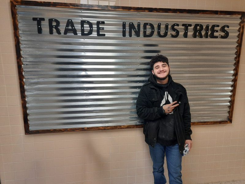 Student Michael Grecco  posing by Trade Industries sign he made