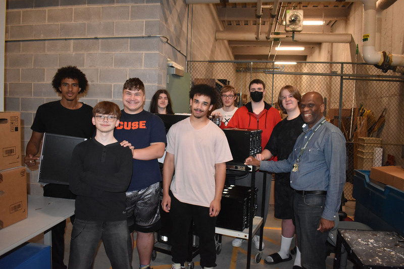 Eight Network Administration students and instructor posing in storage room with computer equipment