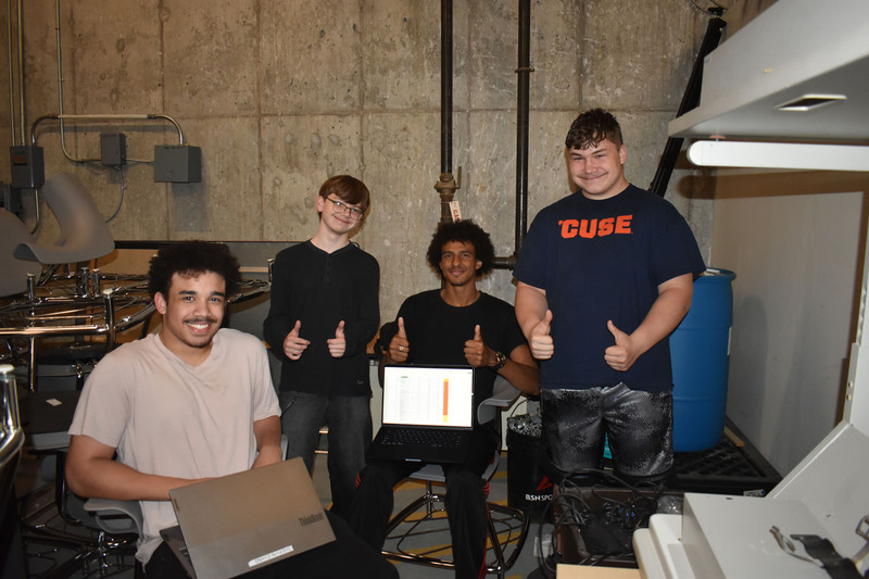 Four Network Administration students posing in storage room with computer equipment
