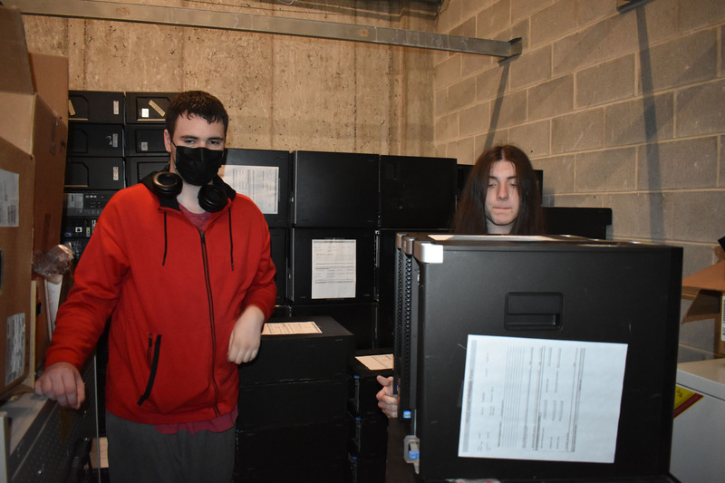 Two Network Administration students moving computers in storage room full of computer equipment