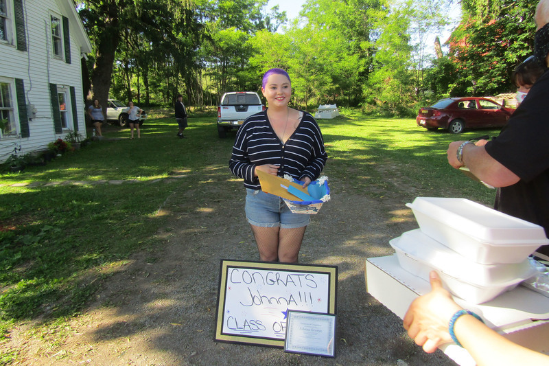 Students next to a sign and a diploma with food about to be handed to her during senior recognition caravan