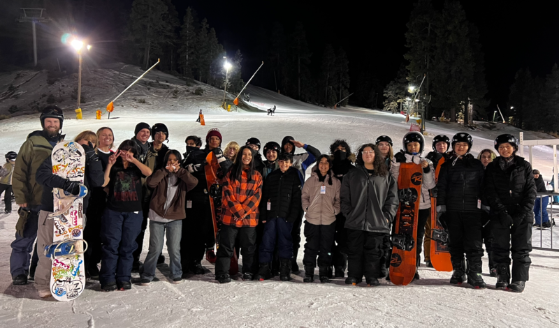 Kids standing in snowboarding gear in the snow.