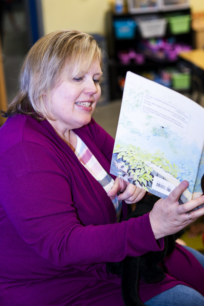 Woman in a purple top holding a book with a garden on the cover, smiling.