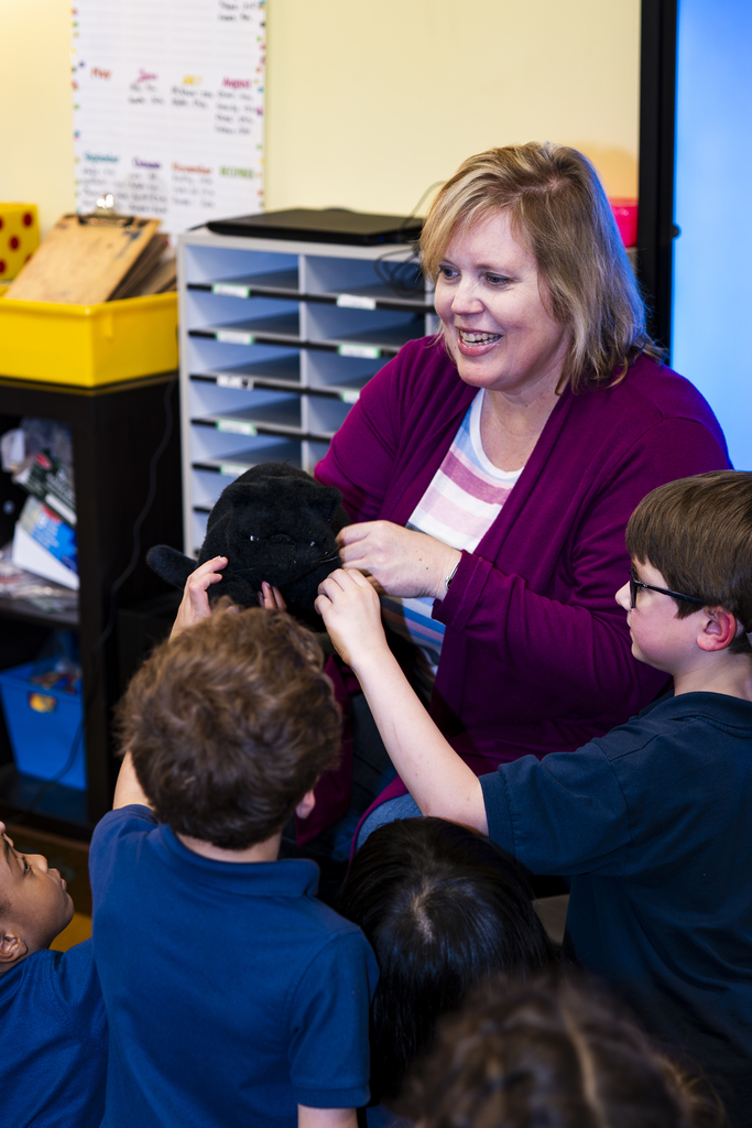 Woman with short hair in purple sweater holding a black dog as children look on.