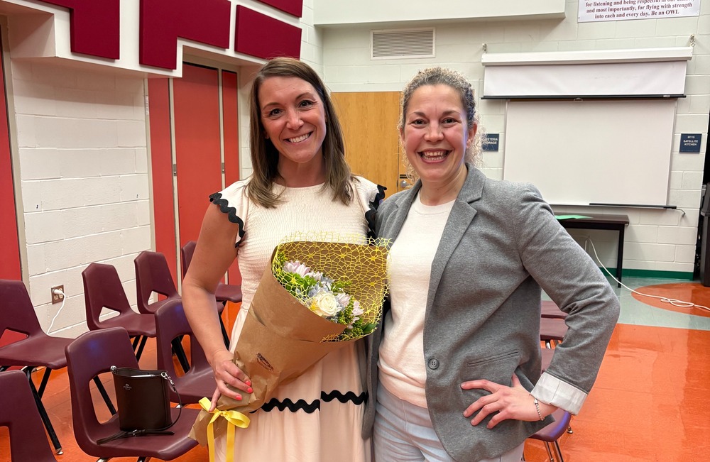 Image is of Ashley Raywood on the left holding flowers as she was welcomed by the Board of Education standing next to Dr. Kristina Susca, Superintendent on her right.