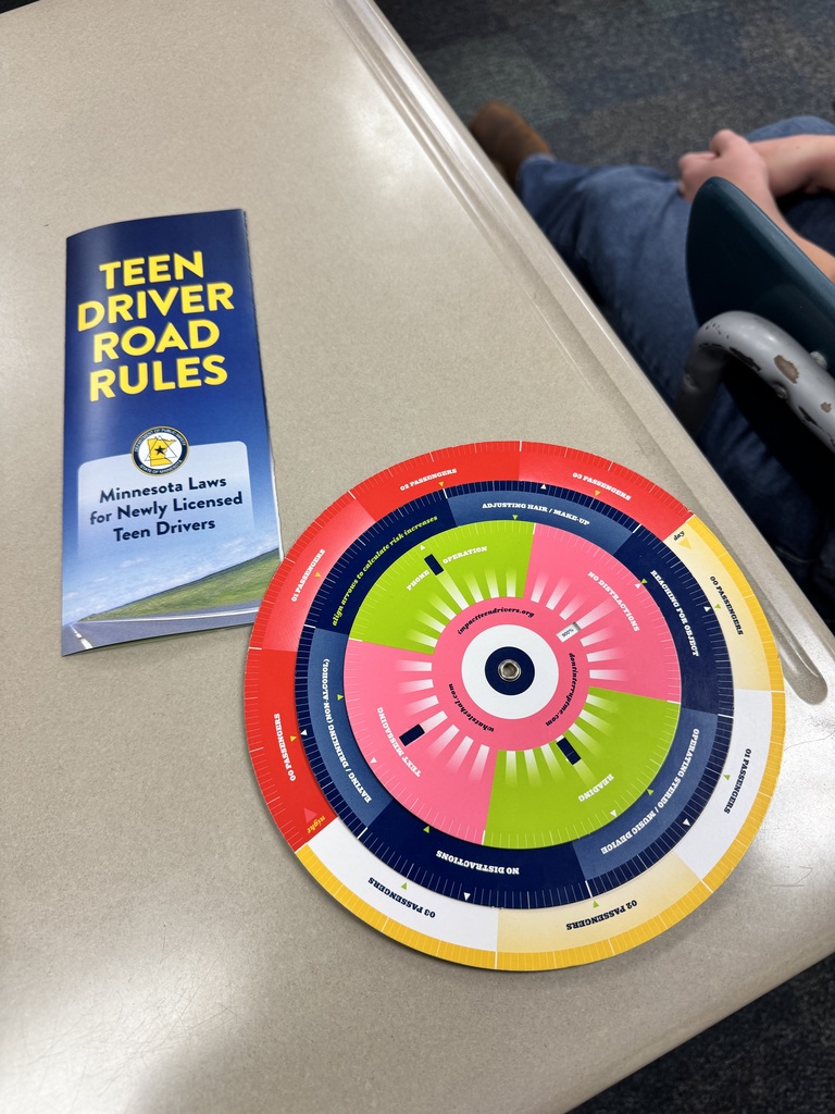 A book titled "Teen Driver Road Rules" and a colorful wheel chart with sections and an arrow are on a table.