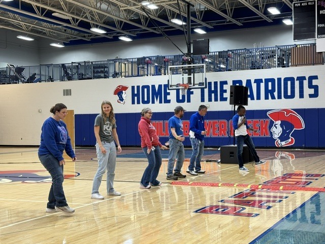 Several people in athletic wear stand on a basketball court. A speaker and microphone are on the right.