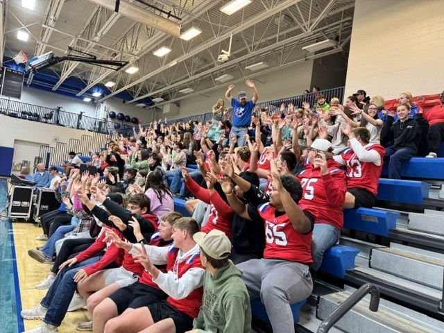 Large audience in a sports stadium with many people wearing red jerseys, some sitting on bleachers, others standing.