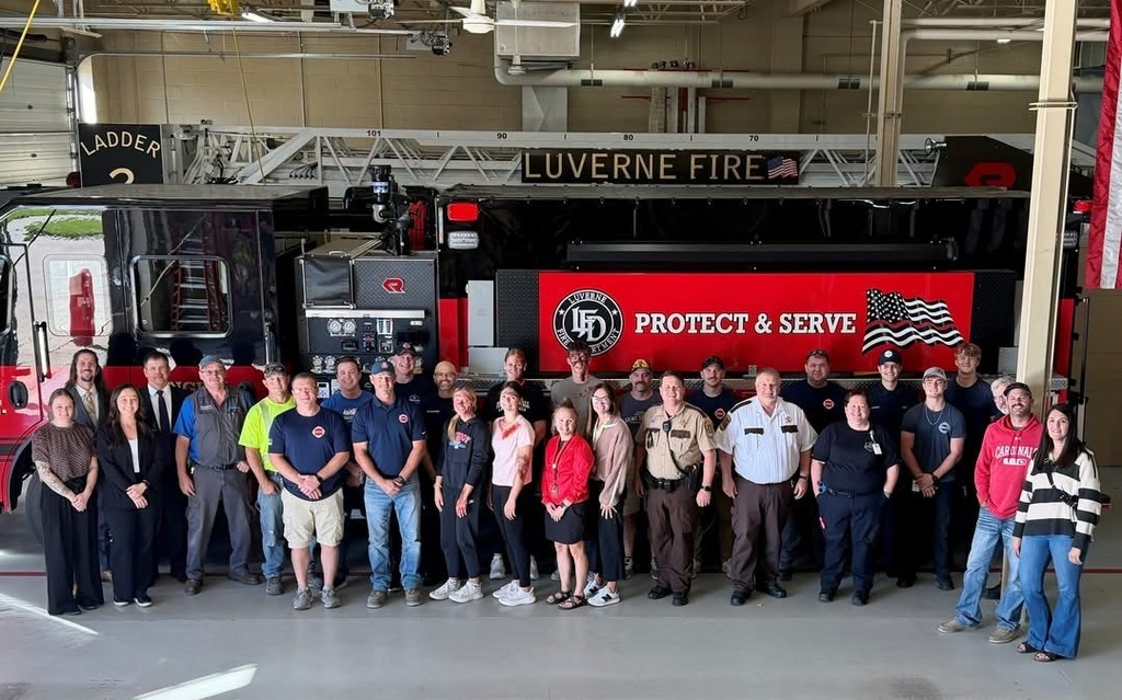 Group of people stand in front of a red fire truck with "Protect & Serve" written on it.