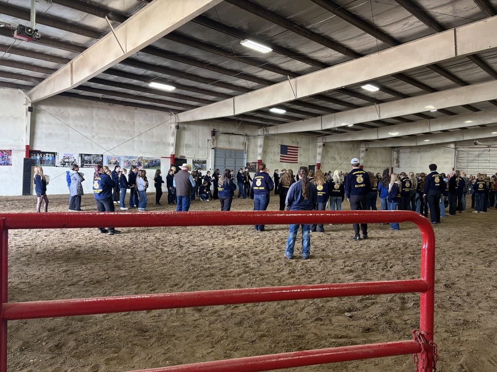 A large group of people in FFA jackets stand in a horse arena with dirt floor.