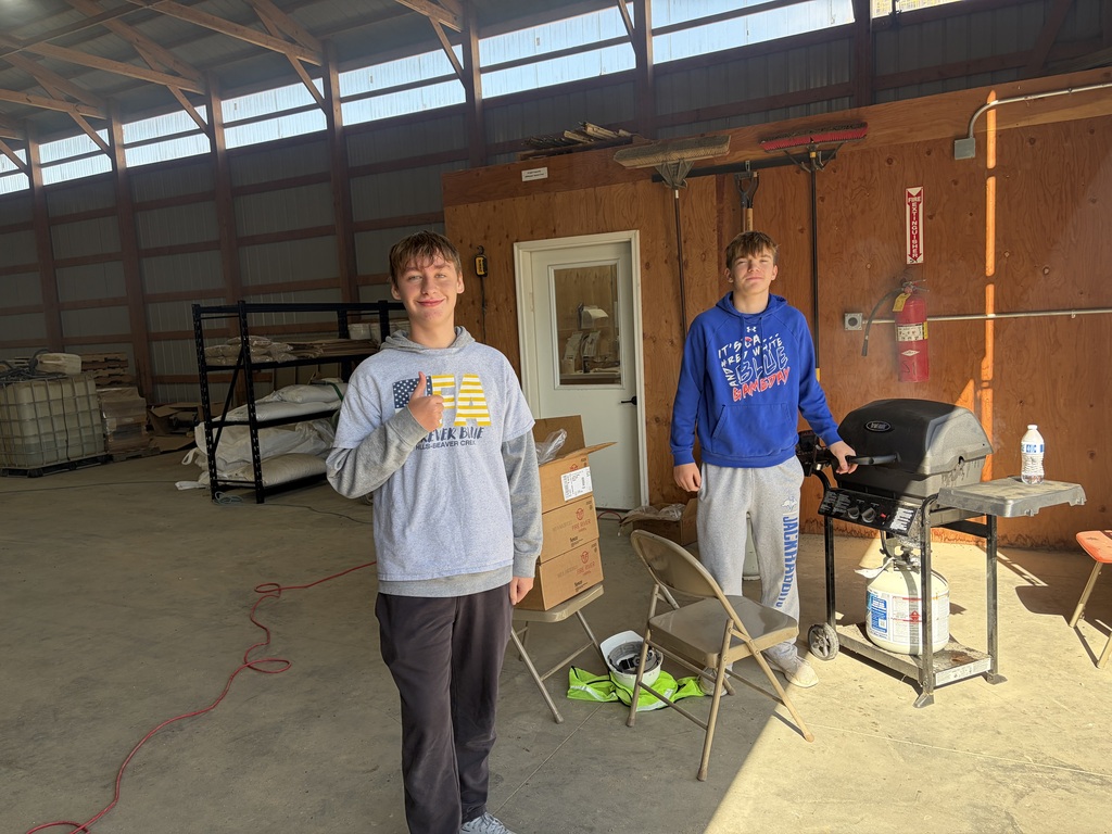 Two young men in a warehouse, one wearing a gray hoodie and the other a blue hoodie. A fire extinguisher is mounted on the wall.