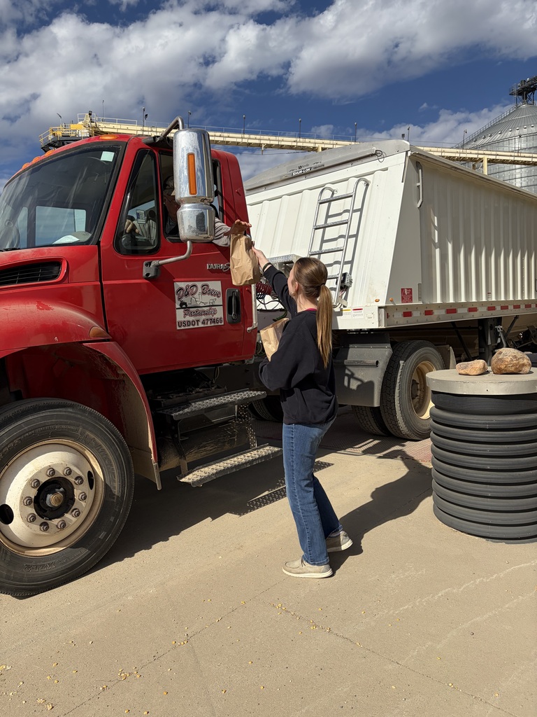 A person hands a bag to a driver of a red semi-truck. The person is wearing a black top and blue jeans.