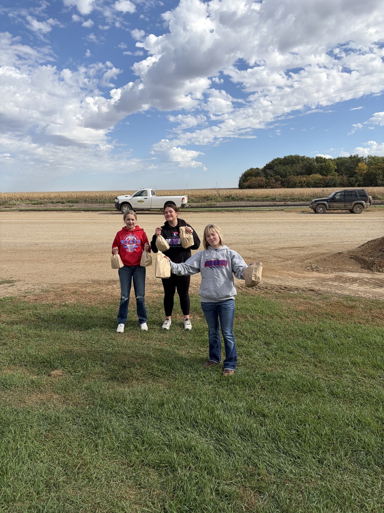 Four people in casual clothes stand in a grassy field with a pickup truck in the background.