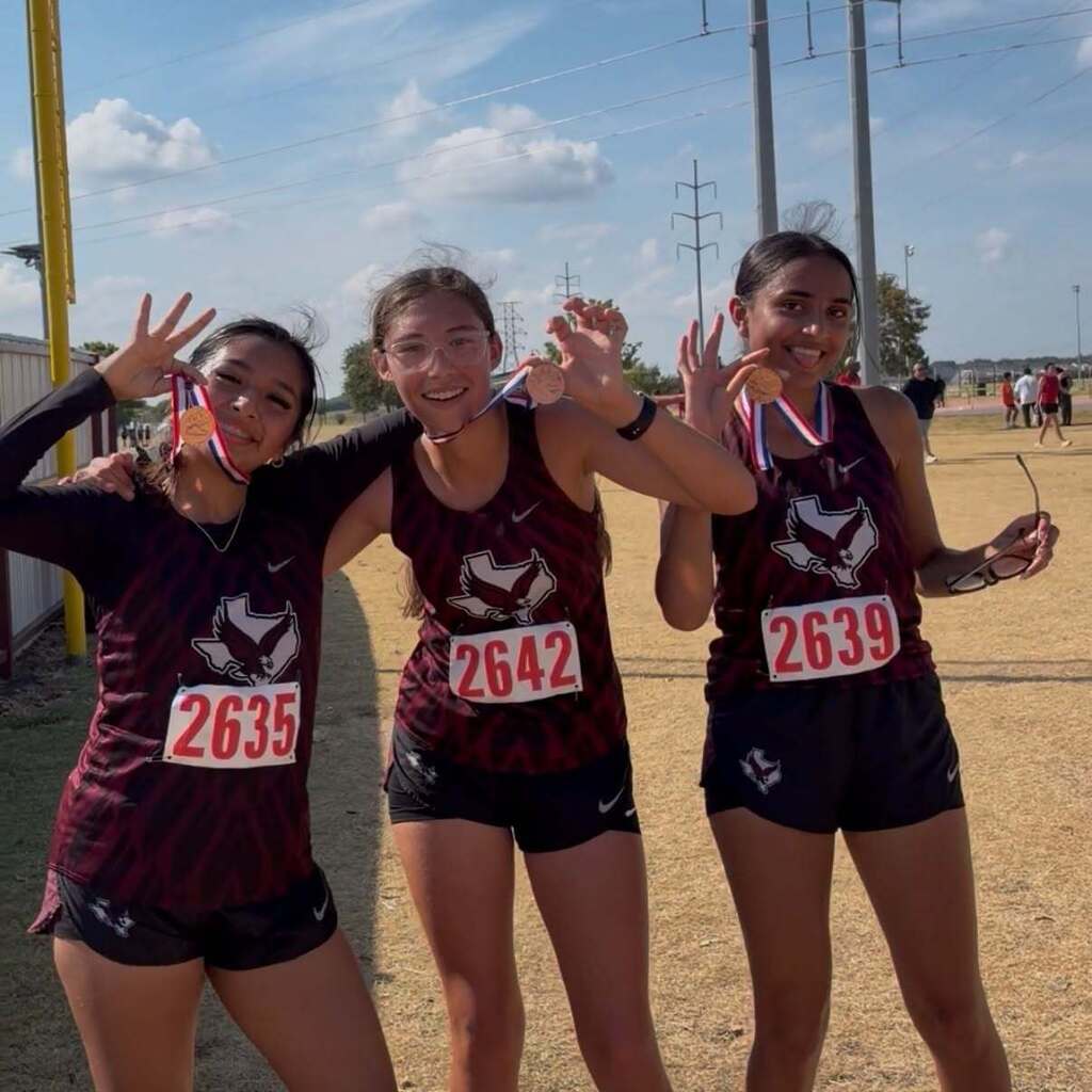 Three cross country students smile with their medal